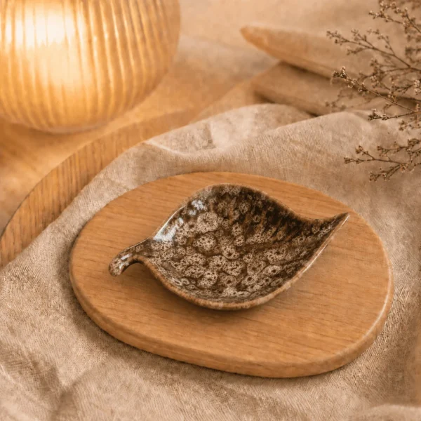 Kastanjebruin keramisch schaaltje in bladvorm met gemĂȘleerd glazuur op een houten plank