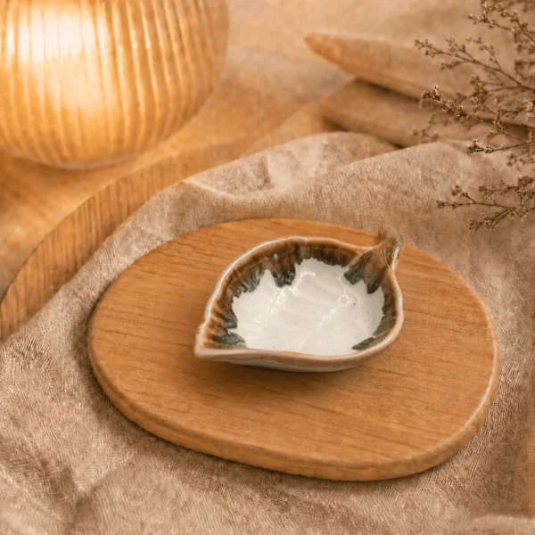 Crème keramisch schaaltje in bladvorm met bruine rand op een houten plank